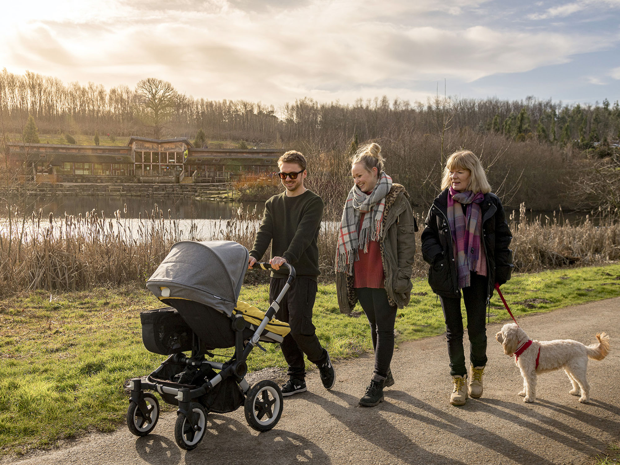 Three adults walking past the lake at Bedgebury Pinetum with a pram and a dog